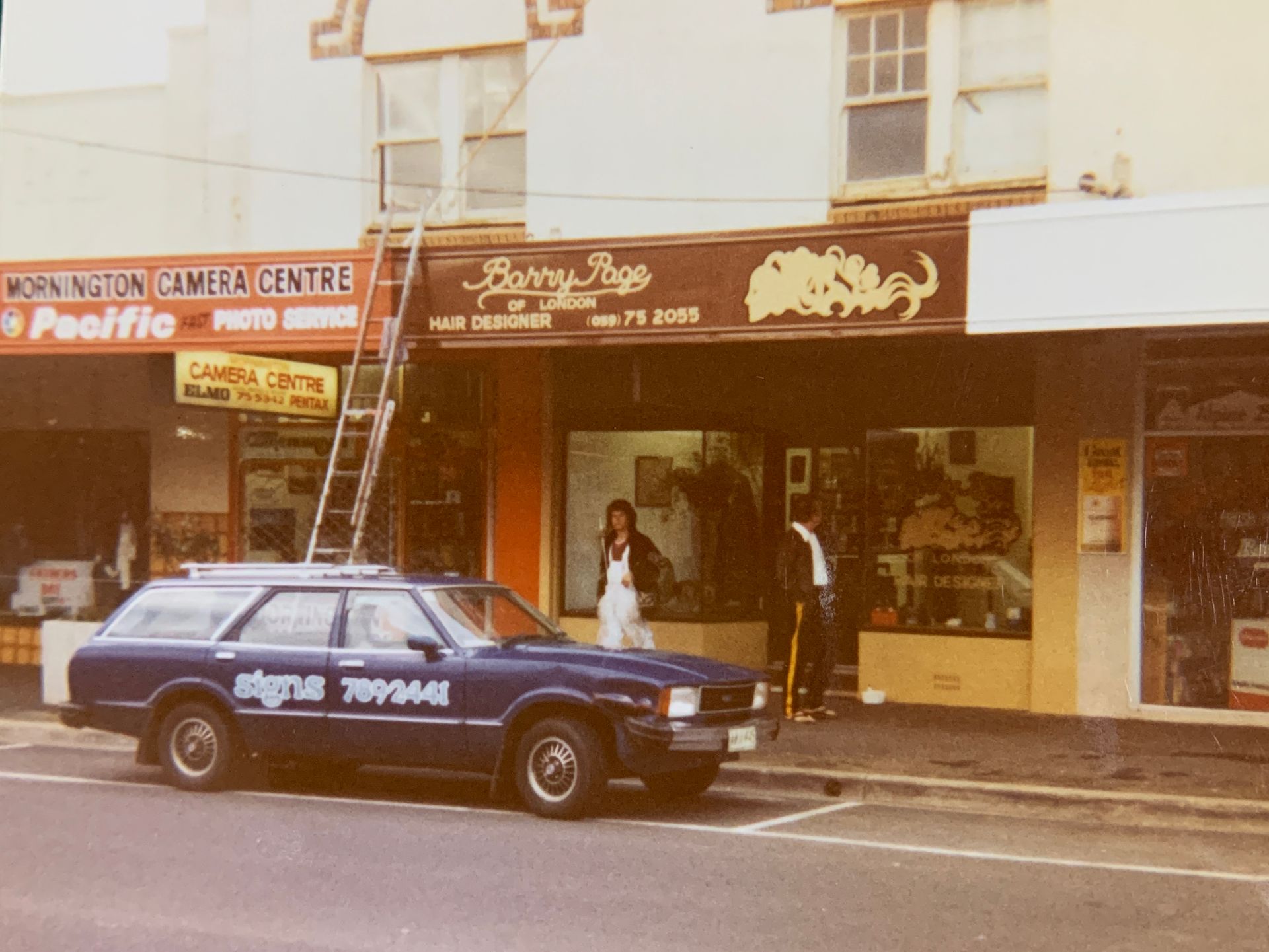 An old photo of a signwriter working above a row of shopfronts.